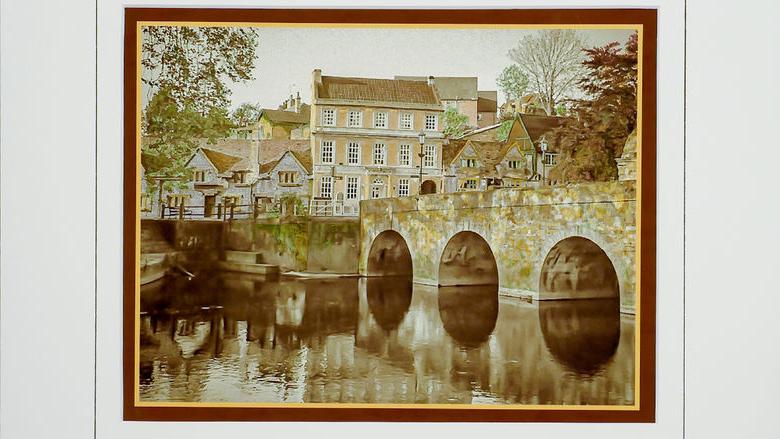 Hand-colored, monochrome photograph of stone bridge and building by 弗兰克Santimauro